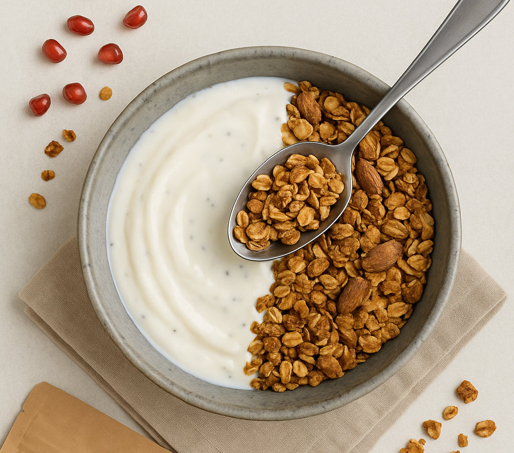 Bol de yaourt nature garni de granola croustillant, présenté en vue du dessus avec une cuillère et quelques graines autour.
