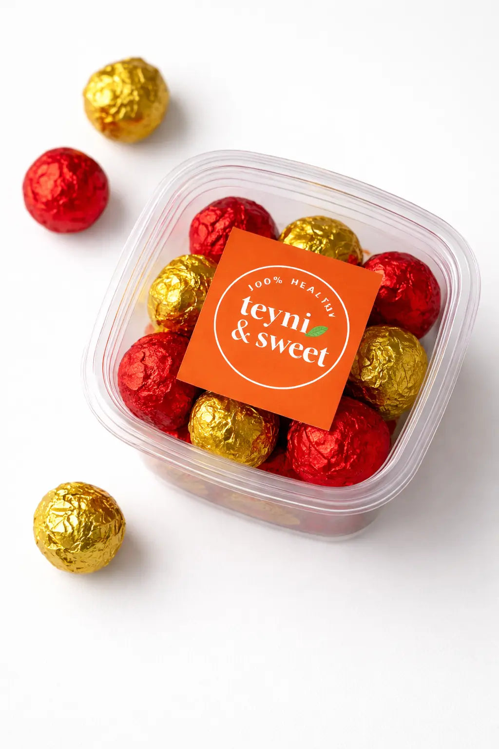 Boîte transparente de boules d’énergie Teyni & Sweet, emballées en papier rouge et doré, présentées sur fond clair.