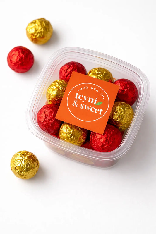 Boîte transparente de boules d’énergie Teyni & Sweet, emballées en papier rouge et doré, présentées sur fond clair.