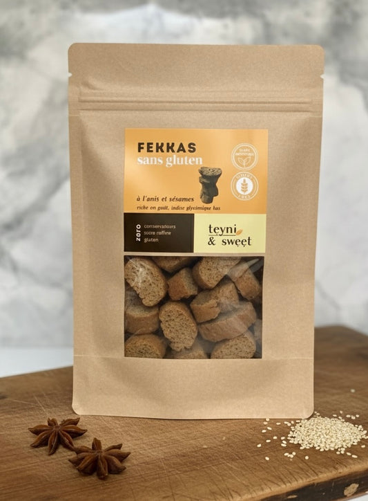 Sachet de fekkas sans gluten à l’anis et sésame Teyni & Sweet sur planche en bois, avec anis étoilé et graines de sésame.